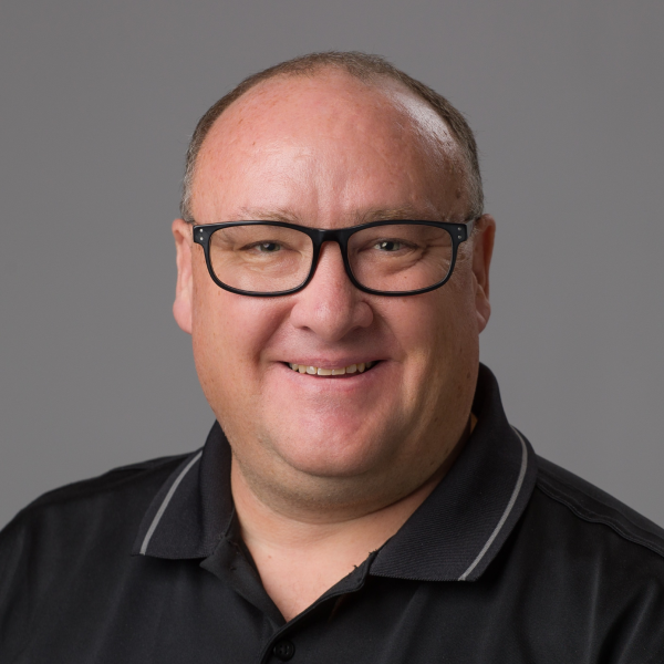 Garth Tuck smiling, wearing glasses and a black polo shirt